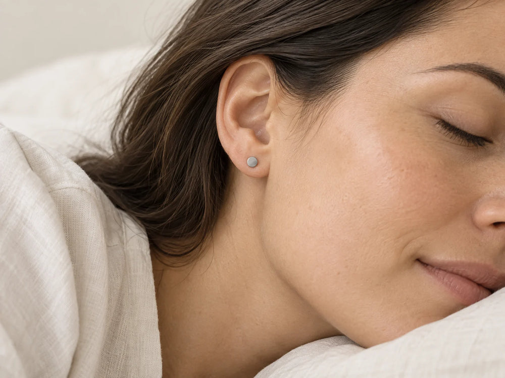 Woman resting on a pillow wearing a small titanium stud earring.